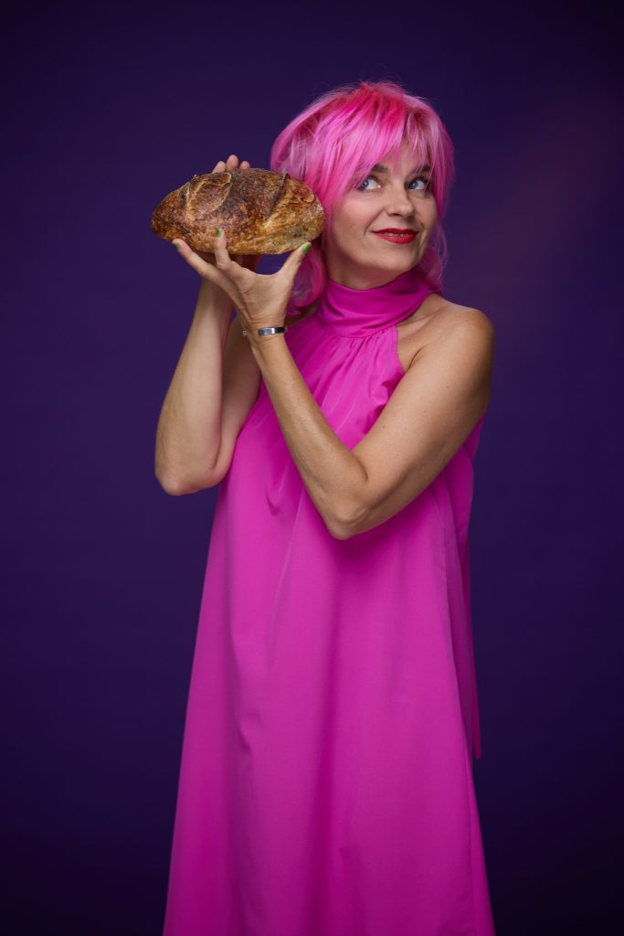 Gianina Corondan, în rochie roz, ține o pâine rotundă lângă ureche