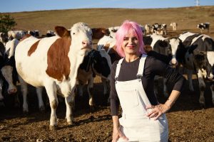 Gianina Corondan, în salopetă albă, între vaci, pe o pajiște